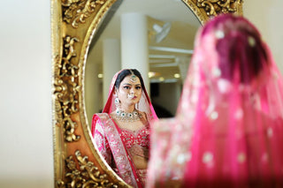 Beautiful bride in traditional Indian attire gazing into an ornate mirror.