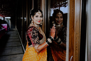Stunning Indian bride in traditional outfit with intricate jewelry and henna, gazing at her reflection.