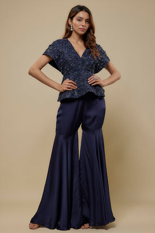 Front view of a navy beaded peplum top with kimono sleeves over a flared satin sharara by Asaga at Mrs. G