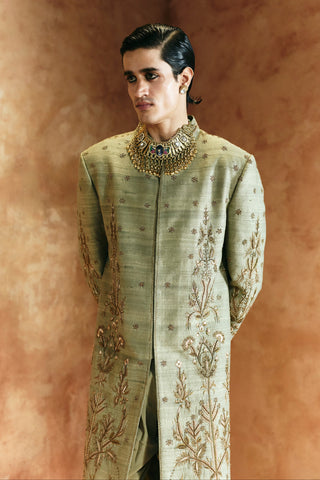Waist-up three-quarter view of the green sherwani set with a statement collar necklace by Aman Takyar at Mrs. G