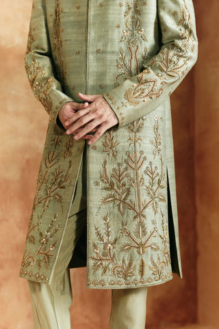 Close-up of the green sherwani set front hem with gold branching zardozi sprays and side slit by Aman Takyar at Mrs. G