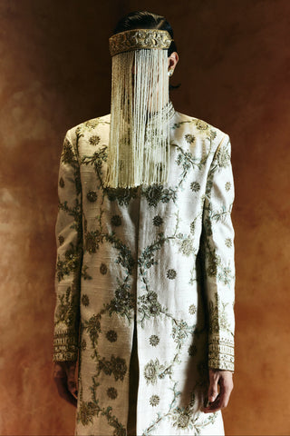 Waist-up close-up of the ivory sherwani chest with gold and sage vines and a pearl veil by Aman Takyar at Mrs. G