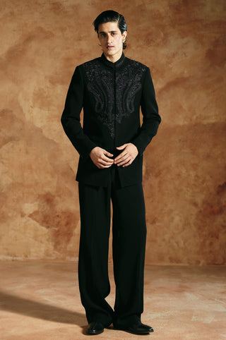 Front view of the black bandhgala set with hands together and flap pockets at the hip by Aman Takyar at Mrs. G