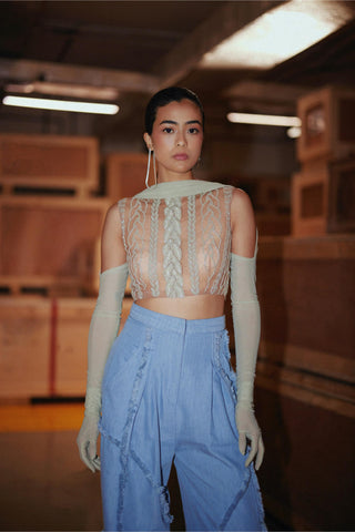 A model stands in a warehouse-like setting wearing a beige lace crop top with matching long gloves and light blue wide-leg pants.