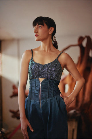 A woman modeling a dark blue sleeveless dress with a textured, patterned lace-like bodice and a structured, gathered corset-style waist with a front zipper.