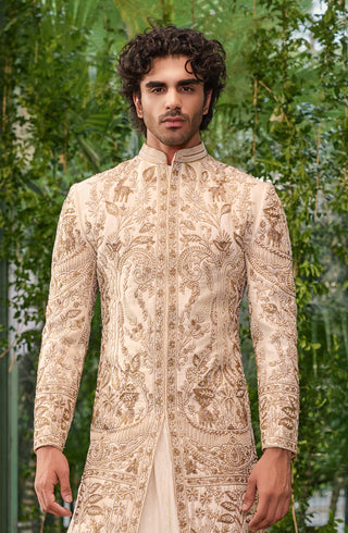 Waist-up front view of the ivory silk sherwani with gold deer and floral vine embroidery and mandarin collar by Jigar and Nikita at Mrs. G