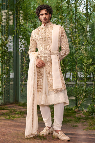 Full-length front view of the ivory cluster sherwani set with gold embroidery, satin dupatta and belt by Jigar and Nikita at Mrs. G