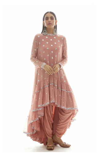 A woman modeling a dusty rose pink traditional Indian outfit with silver mirror work embroidery, paired with matching draped pants and brown shoes, against a solid white background.