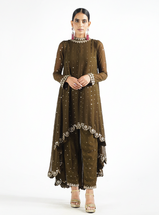 A woman modeling an olive green traditional outfit with silver embellishments, consisting of a long-sleeved tunic and matching pants, against a plain white studio background.