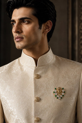 On-model view of the gold and emerald green lion brooch with white stones by Vivinia by Vidhi Mehra worn with a cream sherwani at Mrs. G
