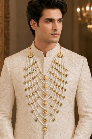 On-model view of the white multi-layer pearl groom mala with gold star motifs by Vivinia by Vidhi Mehra worn with a cream sherwani at Mrs. G
