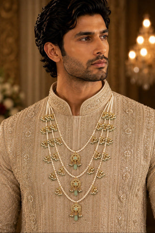 On-model view of the white three-layer pearl kundan groom mala with green drops by Vivinia by Vidhi Mehra worn with a beige embroidered sherwani at Mrs. G
