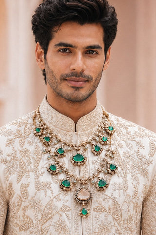 On-model view of the emerald green double-layer kundan statement necklace by Vivinia by Vidhi Mehra worn with a ivory embroidered sherwani at Mrs. G