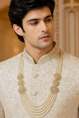 On-model view of the white multi-layer pearl groom mala with gold medallions by Vivinia by Vidhi Mehra worn with a cream sherwani at Mrs. G