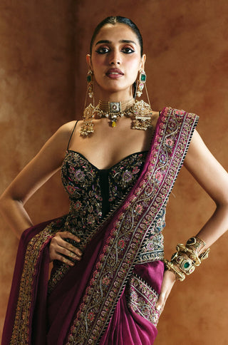 Knee-up view with hands on hips showing the black corset blouse and the magenta saree's pleated drape by Aman Takyar at Mrs. G