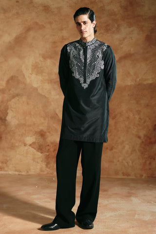 Full-length view of the black kurta set with hands behind the back and wide straight trousers by Aman Takyar at Mrs. G