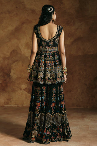 Back view of the black peplum top with scooped back and embroidered hem over the wide sharara by Aman Takyar at Mrs. G