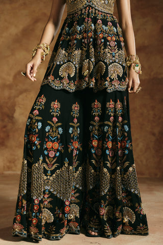 Close-up of the black sharara's tall floral vines and geometric gold border below the peplum hem by Aman Takyar at Mrs. G