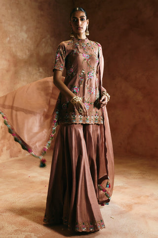Full-length view of the bronze sharara set with the tasseled dupatta corner flowing out to the side by Aman Takyar at Mrs. G