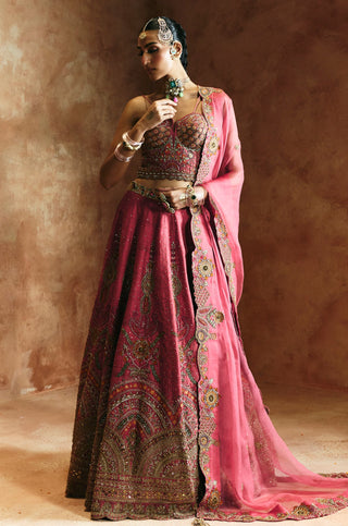 Three-quarter view of the carrot pink lehenga set with one hand raised to the draped dupatta by Aman Takyar at Mrs. G