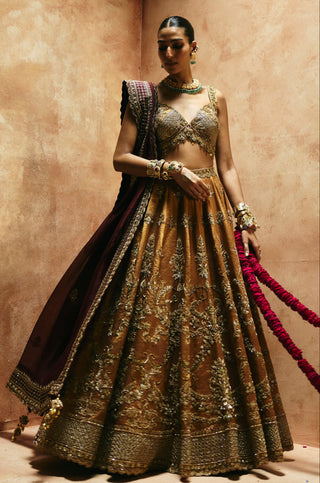 Three-quarter view of the copper gold lehenga with the wine dupatta draped over one arm by Aman Takyar at Mrs. G
