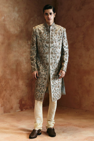 Full-length front view of the dull green sherwani set with embroidered front and cream churidar by Aman Takyar at Mrs. G