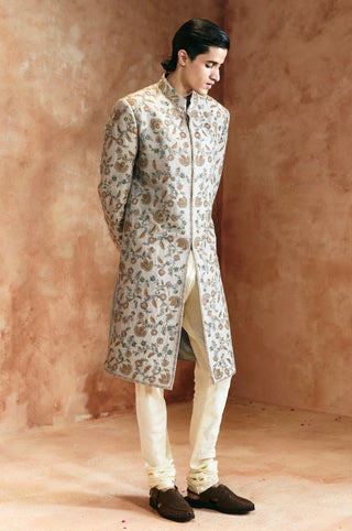 Full-length view of the dull green sherwani with the head turned down and embroidery along the sleeves by Aman Takyar at Mrs. G