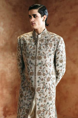 Waist-up side view of the dull green sherwani with hands behind the back and the stand collar by Aman Takyar at Mrs. G