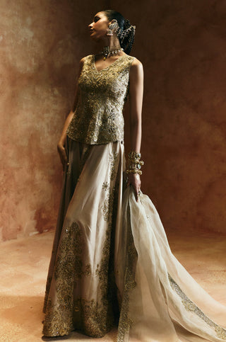 Angled view of the gold peplum top and sharara with the long dupatta trail by Aman Takyar at Mrs. G