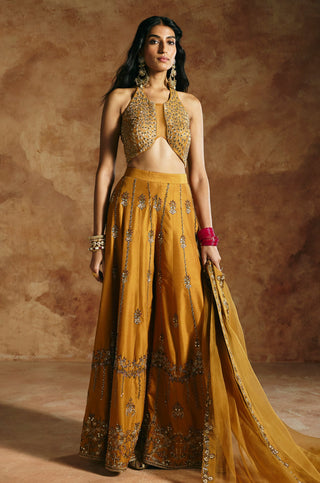 Front view of the mustard halter top and wide sharara with the dupatta draped to one side by Aman Takyar at Mrs. G