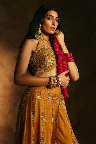 Three-quarter close-up of the mustard halter top and sharara with a pink flower garland by Aman Takyar at Mrs. G