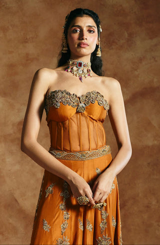 Full-length view of the orange corset and sharara set with hands clasped and the embroidered hem by Aman Takyar at Mrs. G