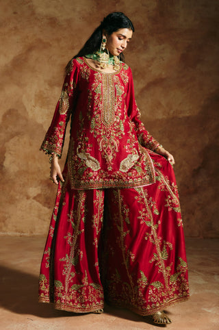 Three-quarter view of the red sharara flaring out with floral vines along the embroidered hem by Aman Takyar at Mrs. G