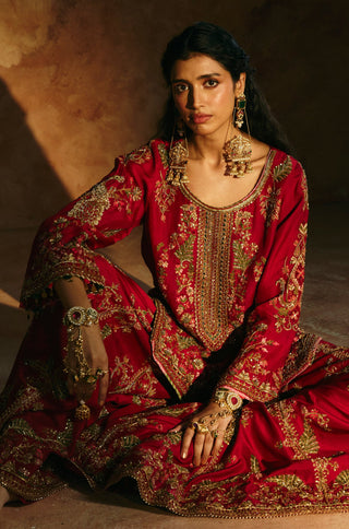 Seated view of the red sharara set with the heavily embroidered hem spread out by Aman Takyar at Mrs. G