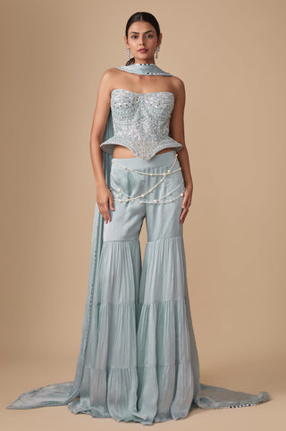 Full-length front view of the baby blue strapless mirror work corset with the three-tier sharara, pearl waist strands and trailing dupatta by Asaga at Mrs. G