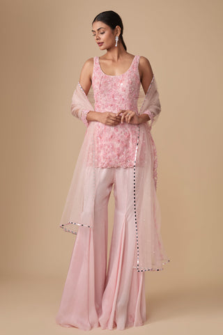 Full-length front view of the baby pink sleeveless floral short kurti with gored satin sharara and mirror-border net dupatta by Asaga at Mrs. G
