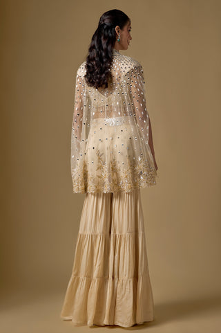 Back view of the beige sheer cape with mirrors and a scalloped gold floral hem over the tiered sharara by Asaga at Mrs. G