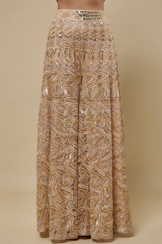 Waist-down view of the beige sharara with looping gold scroll embroidery and a mirror work waistband by Asaga at Mrs. G