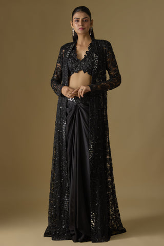 Full-length front view of a black floor-length net jacket over a floral blouse and draped satin skirt by Asaga at Mrs. G