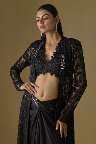 Waist-up view of the black scalloped floral V-neck blouse under a mirror panel net jacket by Asaga at Mrs. G