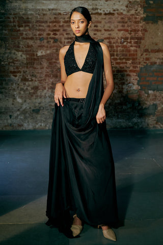 Front view of a black pre-draped saree with a halter blouse and a knotted satin hip drape by Asaga at Mrs. G
