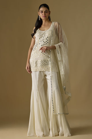 Front view of an ivory mirror work kurti with a net dupatta over a flared satin sharara by Asaga at Mrs. G