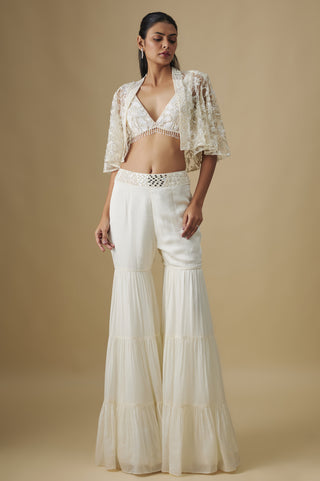 Front view of an ivory tiered sharara set with a V-neck blouse and a floral net cape by Asaga at Mrs. G
