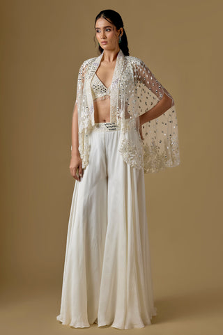 Full-length front view of the ivory short mirror cape with slit sleeves over a bralette blouse and wide satin sharara by Asaga at Mrs. G