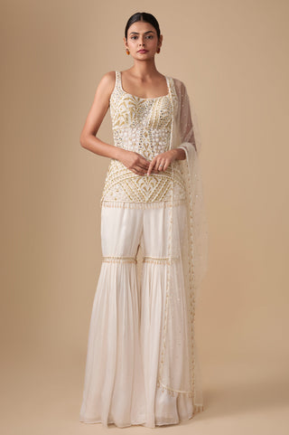 Full-length front view of the ivory gold sleeveless embroidered short kurti with gathered sharara and net dupatta by Asaga at Mrs. G