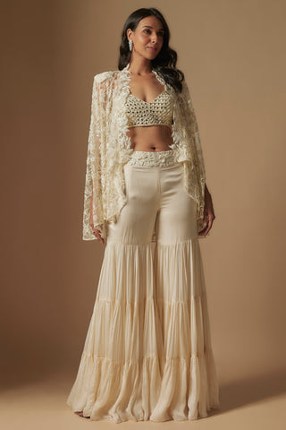 Front view of an ivory mirror work blouse under an open sheer embroidered cape with a tiered sharara by Asaga at Mrs. G
