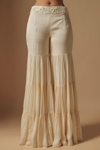 Waist-down view of the ivory tiered sharara with a raised leaf embroidered waistband by Asaga at Mrs. G