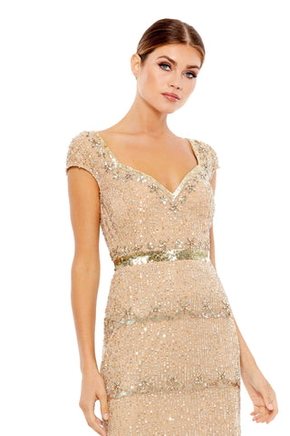 Waist-up view of the champagne beaded cap sleeve column gown showing the sweetheart neckline and gold sequin belt by Mac Duggal at Mrs. G