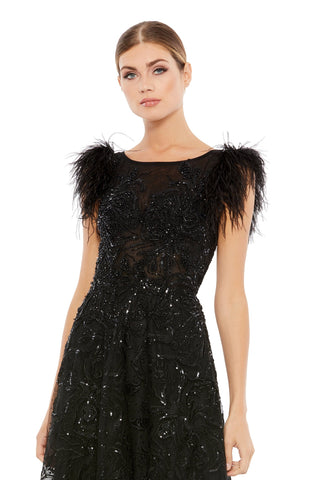 Waist-up view of the black feather cap sleeve embellished A line gown showing the feather trimmed shoulders over a beaded illusion bodice by Mac Duggal at Mrs. G