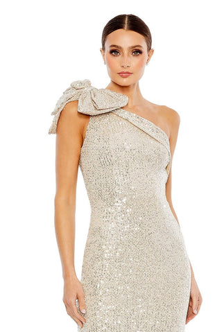 Waist-up view of the champagne sequined one shoulder bow column gown showing the sequined bow at the shoulder and fitted bodice by Mac Duggal at Mrs. G